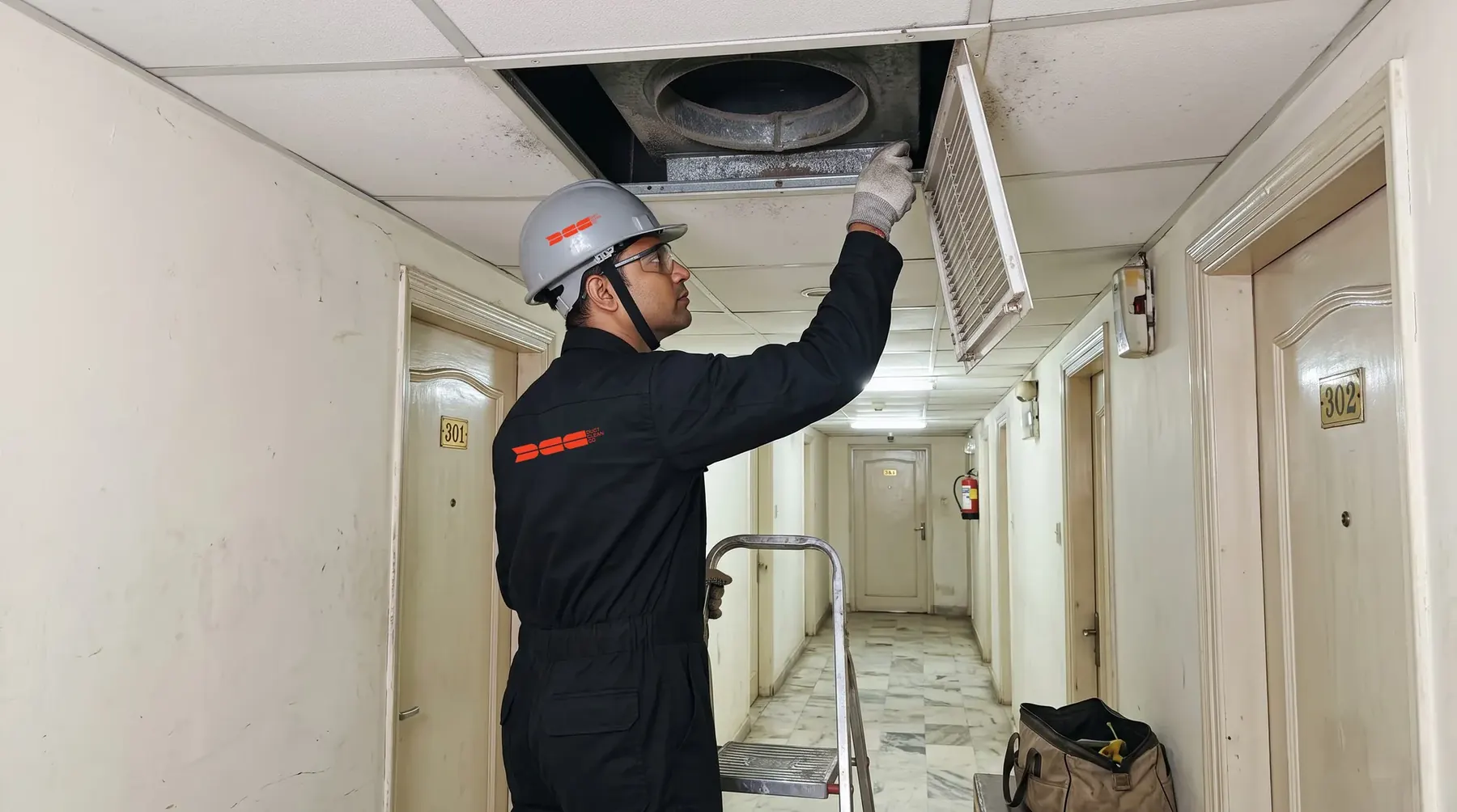 DCC technician opening a ceiling grille on a guest-floor corridor during zone-wise execution